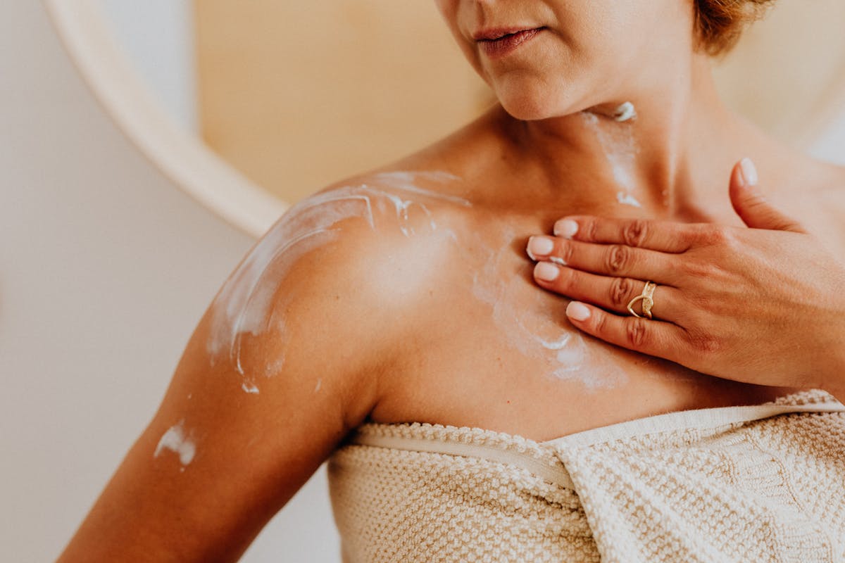 Close-up of a woman applying moisturizing cream to her shoulder indoors, promoting skincare routine.