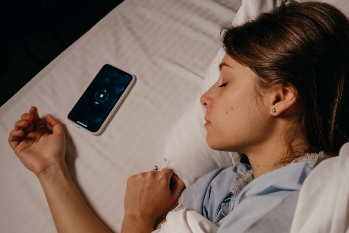 A woman sleeping peacefully in bed beside her smartphone, capturing a serene bedtime moment.