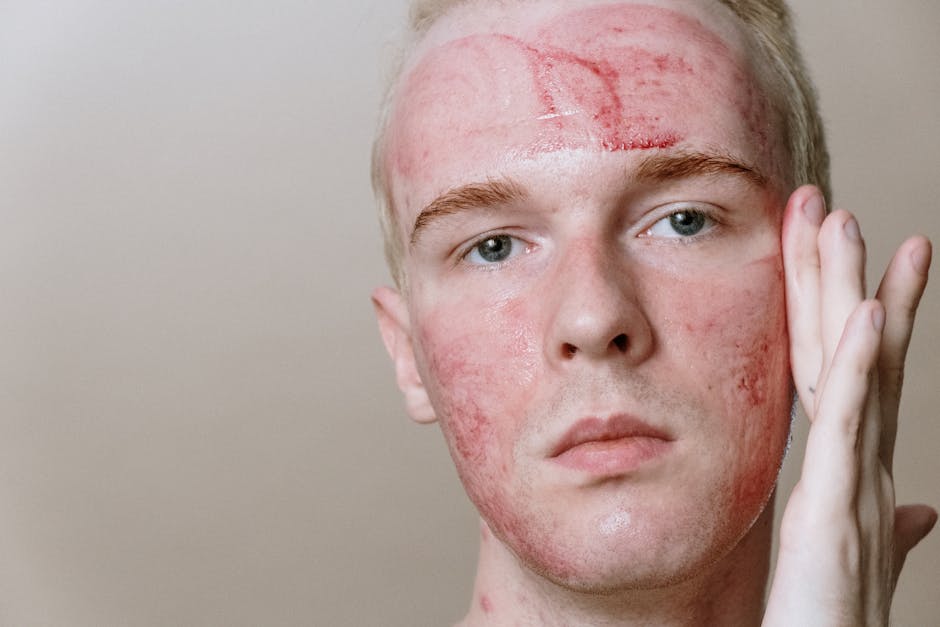 Mężczyzna z podrażnioną skórą na twarzy, dotykający policzka. Widoczne zaczerwienienia i nierówności na skórze, co sugeruje problemy dermatologiczne. Naturalne oświetlenie, neutralne tło.