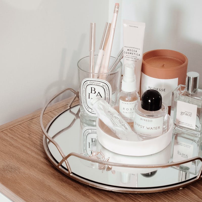 Stylish arrangement of beauty products on a wooden table with a mirror tray, creating an aesthetic display.